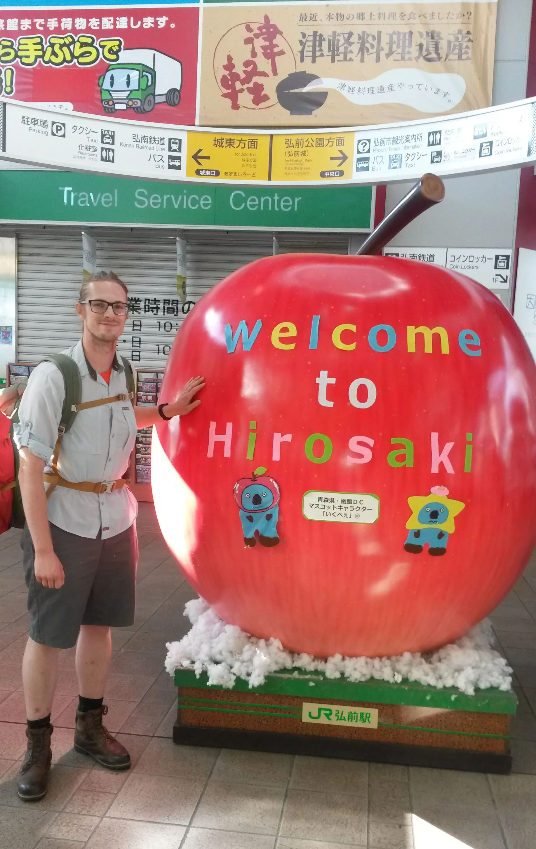 Mężczyzna przy dużym, sztucznym, czerwonym jabłku na dworcu w Hirosaki