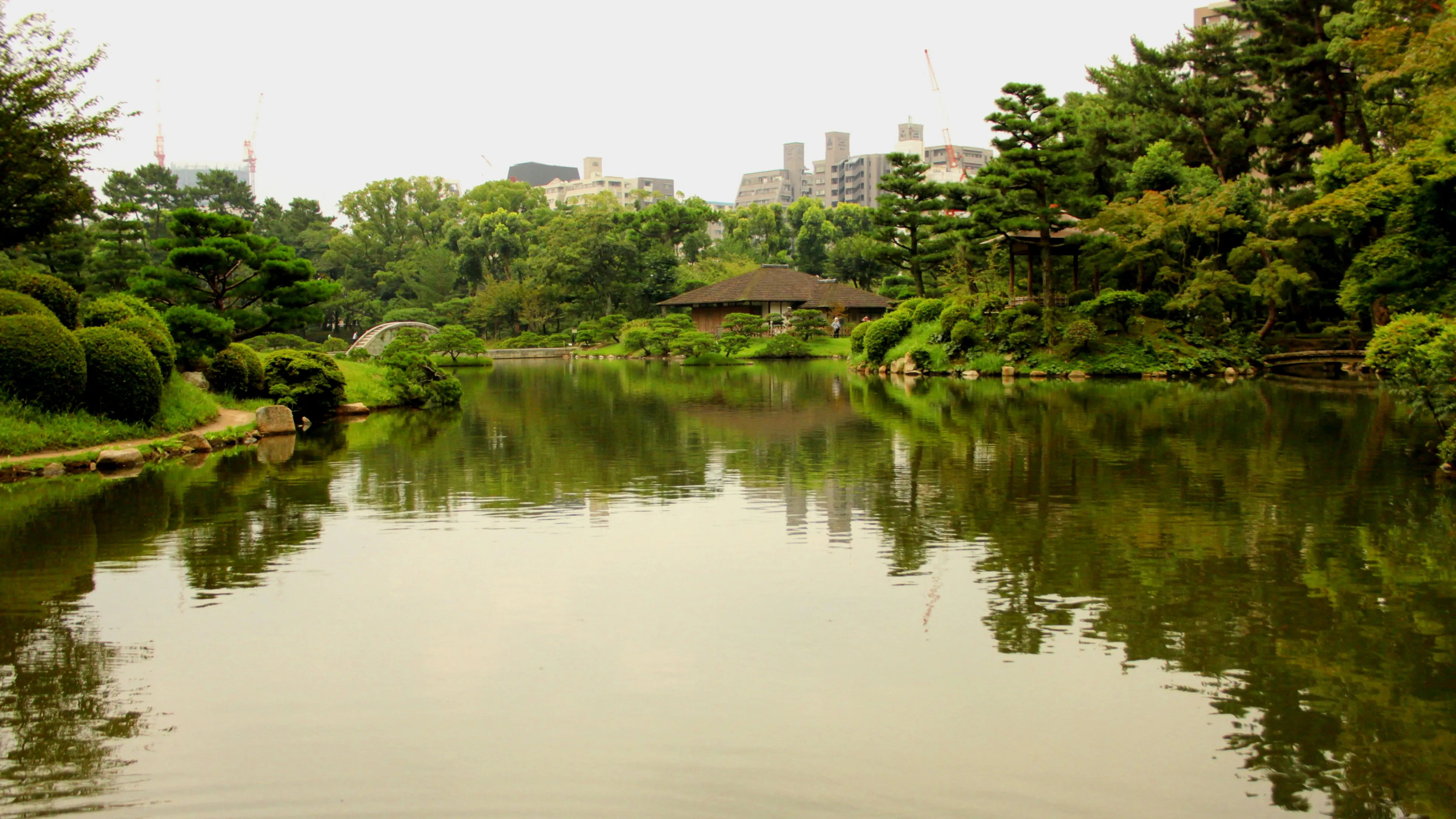 Image of a serene pond in Shukkeien Park, surrounded by lush greenery and traditional Japanese landscaping.