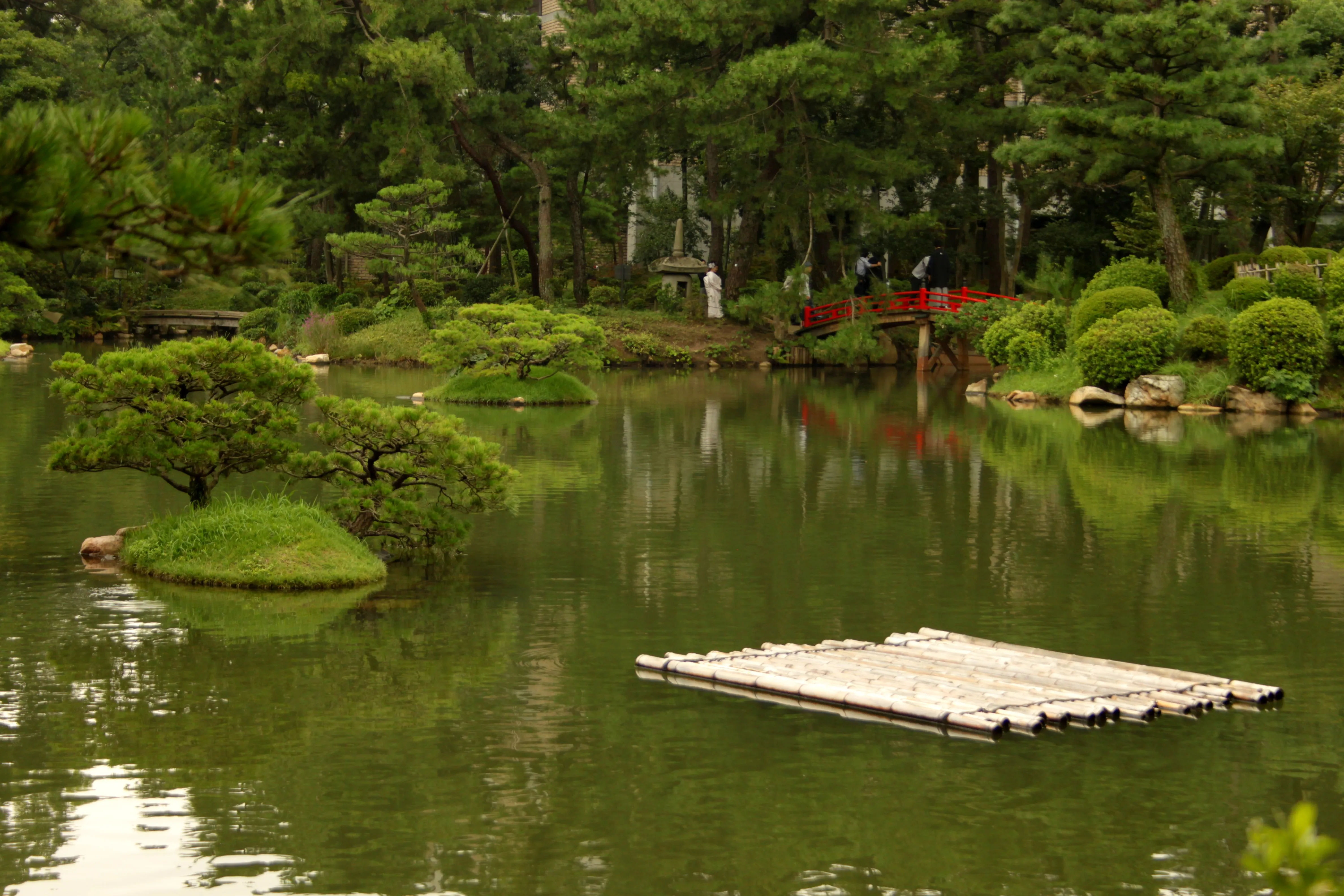 Image of a red bridge in Shukkeien Park, crossing over a calm pond with meticulously maintained greenery.