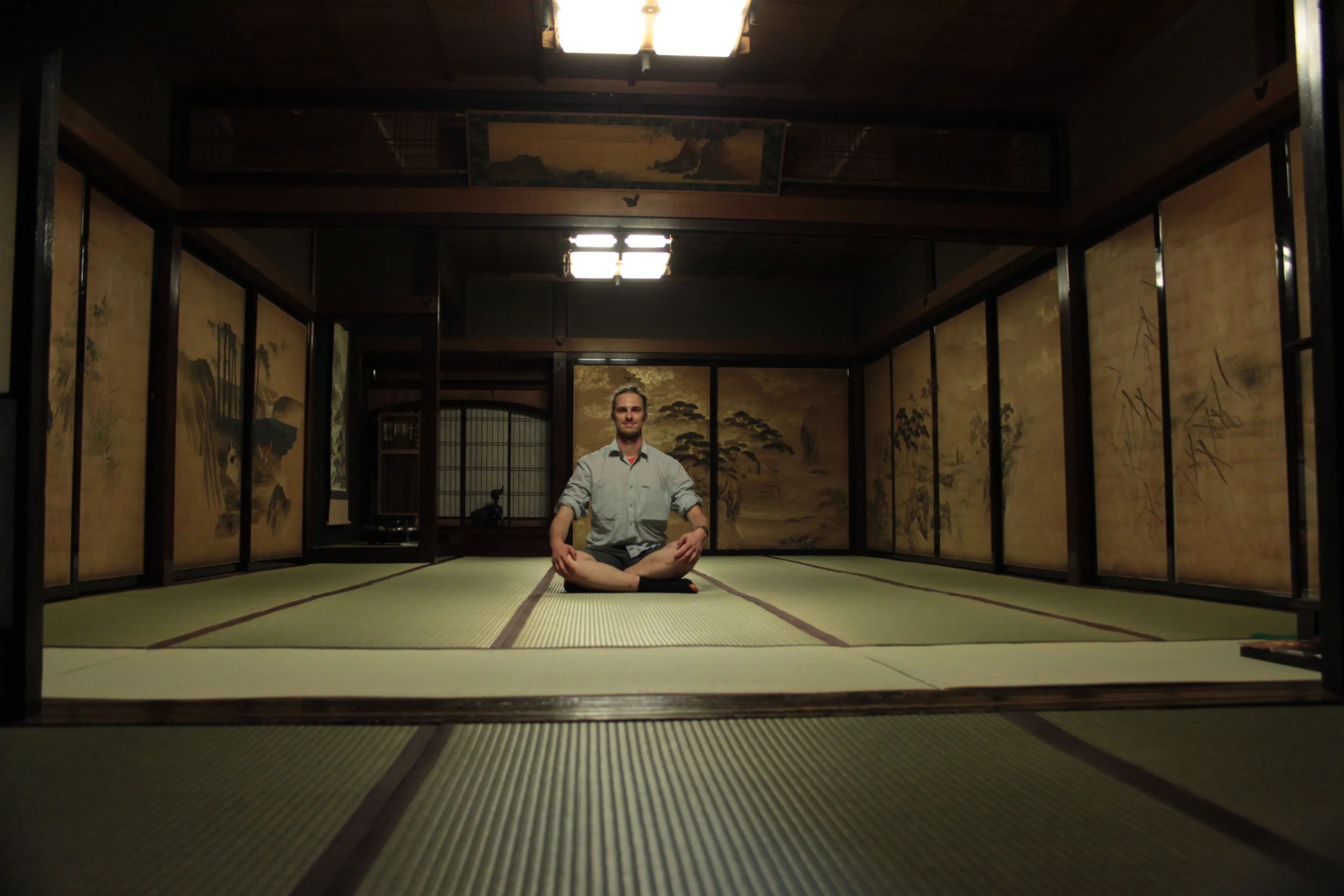 Mężczyzna siedzący na podłodze z tatami w tradycyjnym japońskim pokoju z przesuwanymi drzwiami