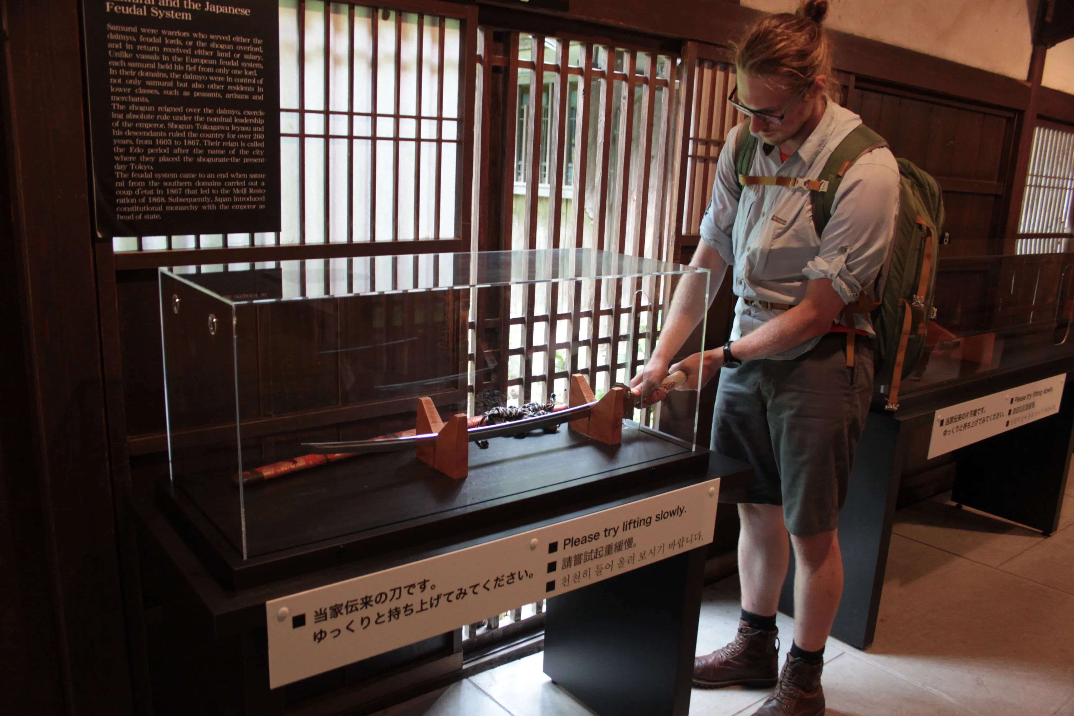 Mężczyzna z plecakiem oglądający tradycyjną japońską broń w gablocie w muzeum
