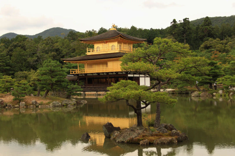 Kinkaku-ji, Złoty Pawilon w Kioto, odbijający się w stawie otoczonym zielenią.