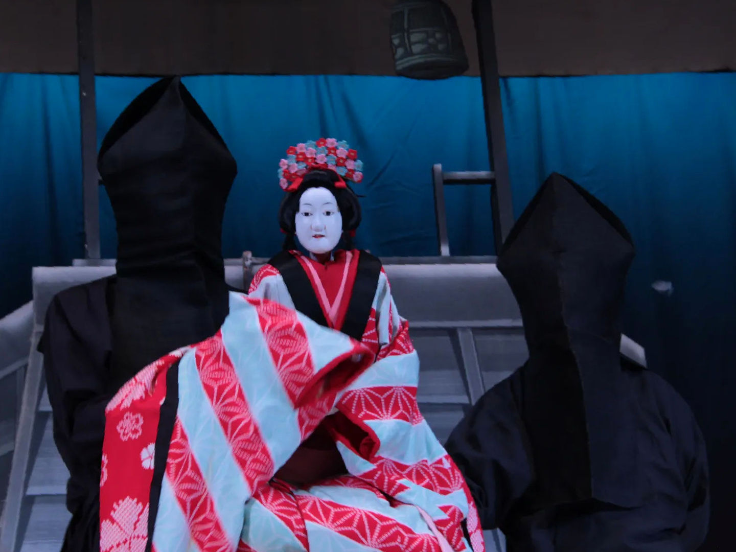 Lalka Bunraku na scenie teatru japońskiego, przedstawiona z dwoma animatoremami.