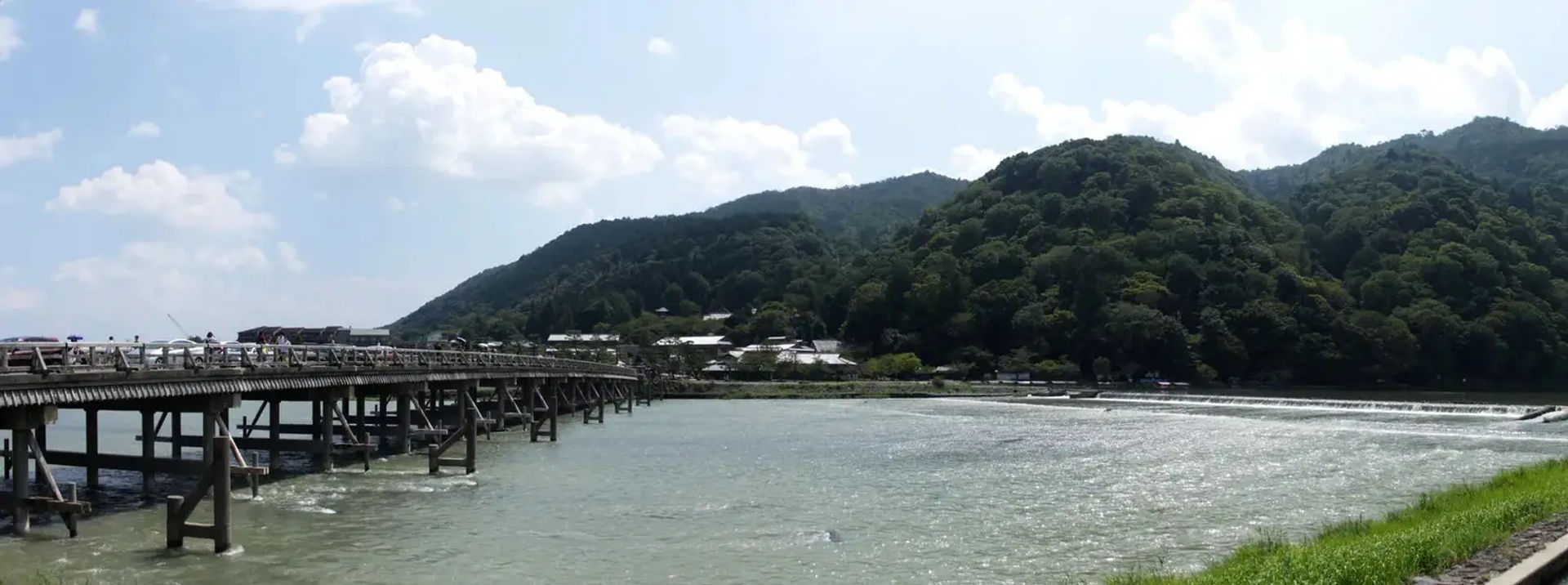 Panorama mostu Togetsukyo nad rzeką w Arashiyamie, Kioto, z górami w tle.