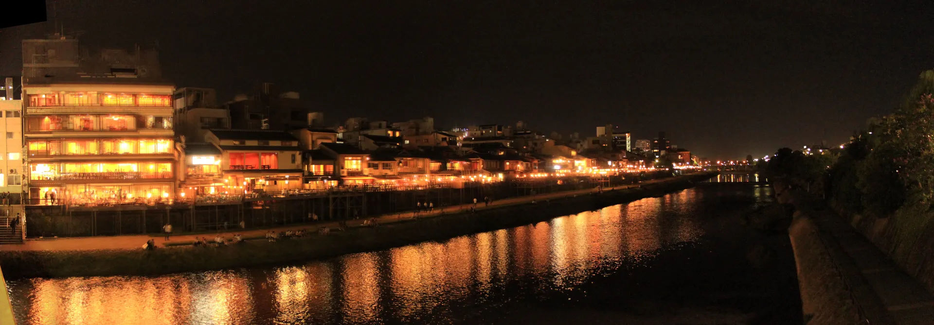 Nocny widok na Pontocho i rzekę Kamogawa w Kioto, oświetlone tradycyjne restauracje nad brzegiem rzeki.