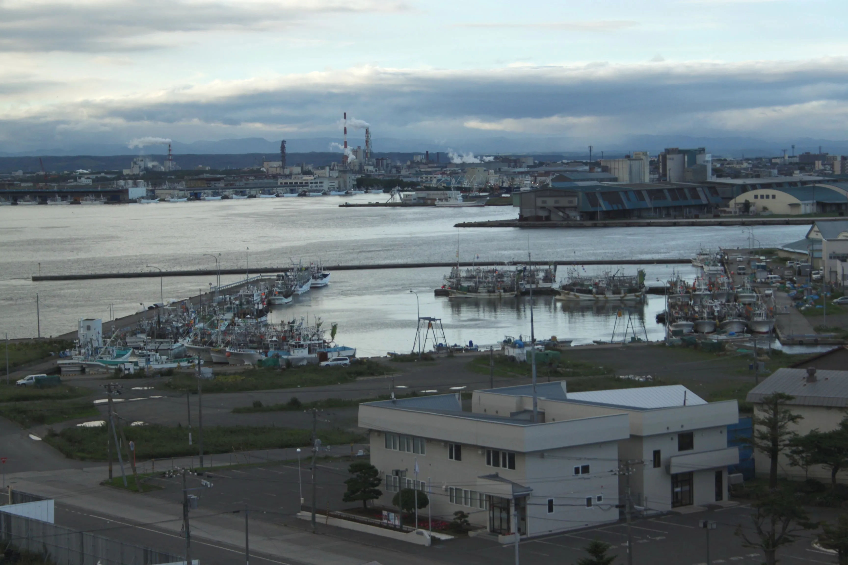 Widok na port w Kushiro z zacumowanymi łodziami, budynkami portowymi i industrialnym tłem