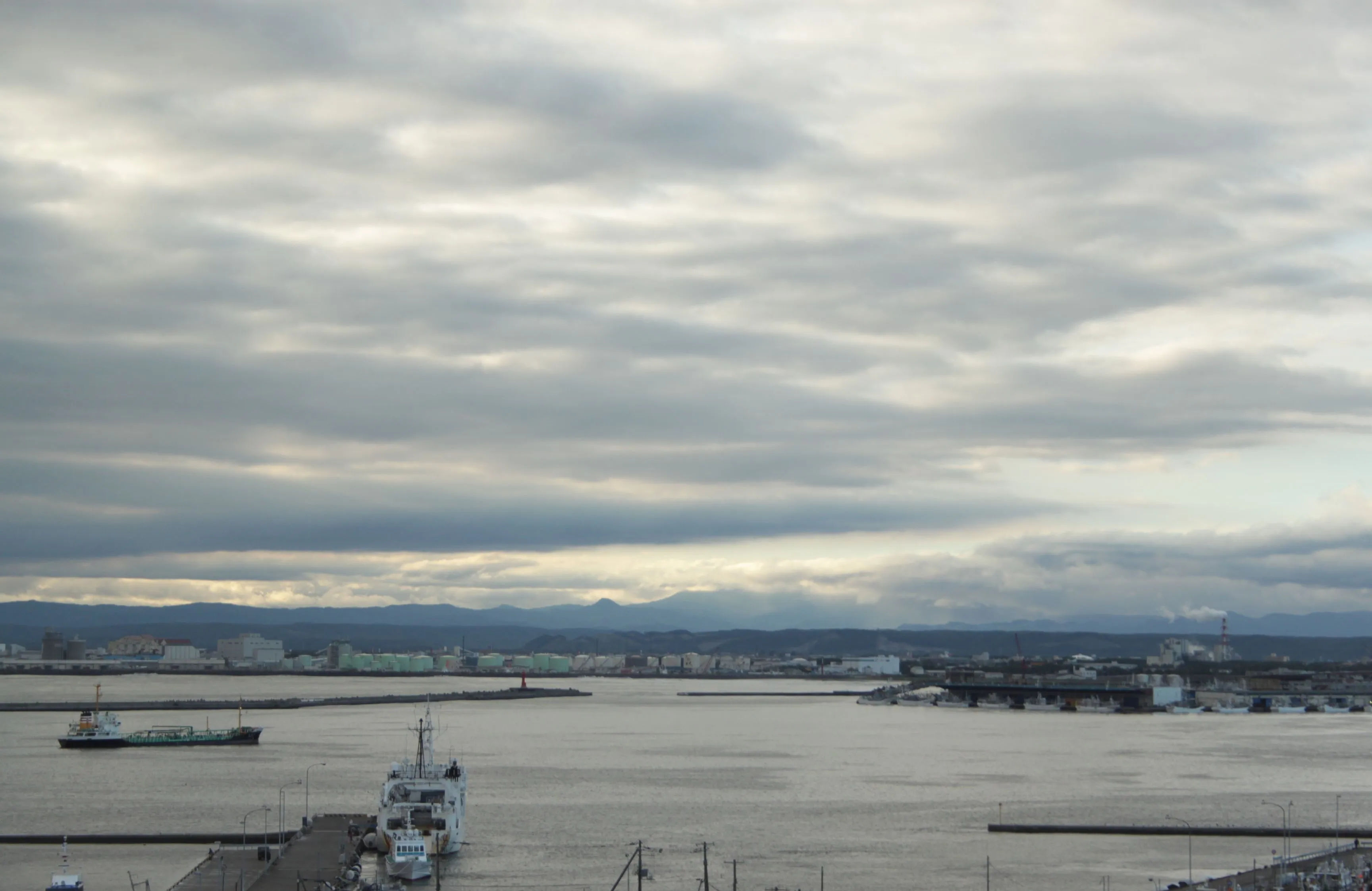 Widok na rozległy port w Kushiro z łodziami na wodzie, pod pochmurnym niebem