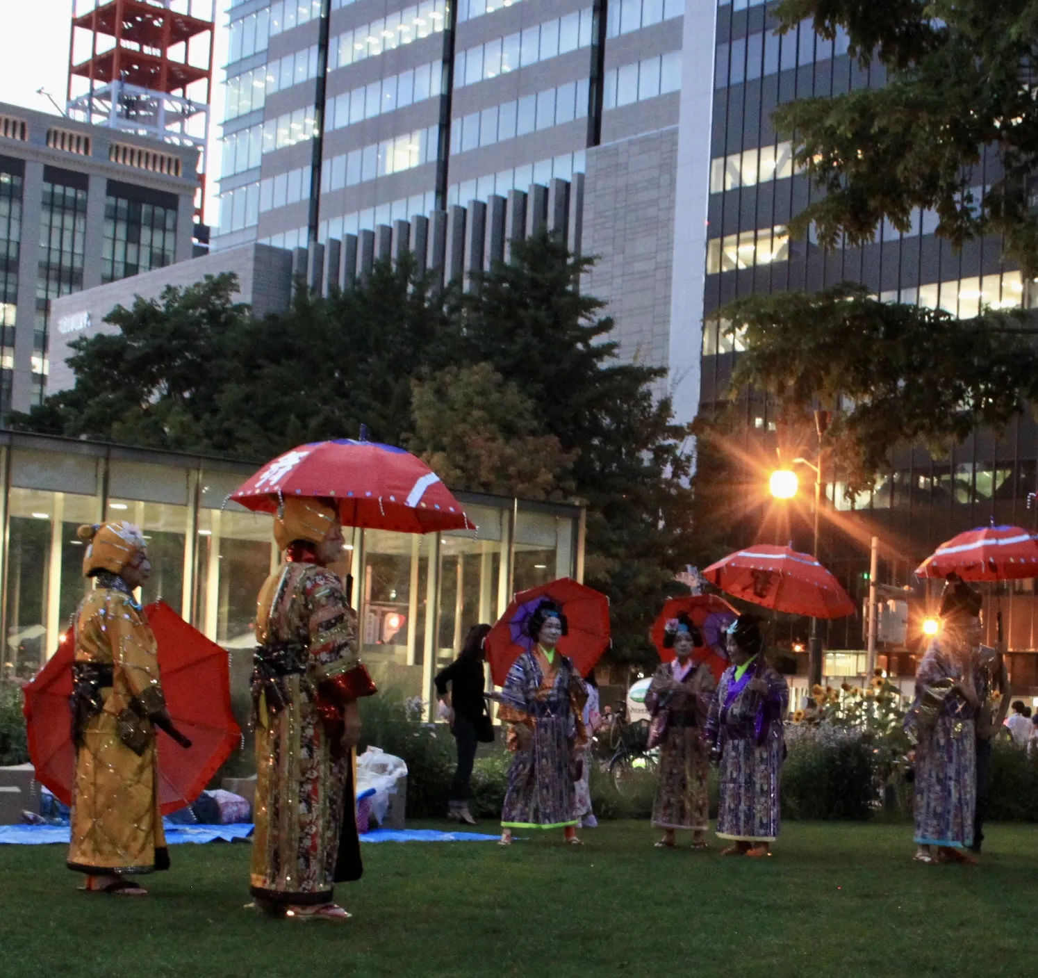 Przygotowania tancerzy do Bon Odori w Parku Odori w Sapporo, ludzie w japońskich strojach z umalowanymi twarzami i czerwonymi parasolami