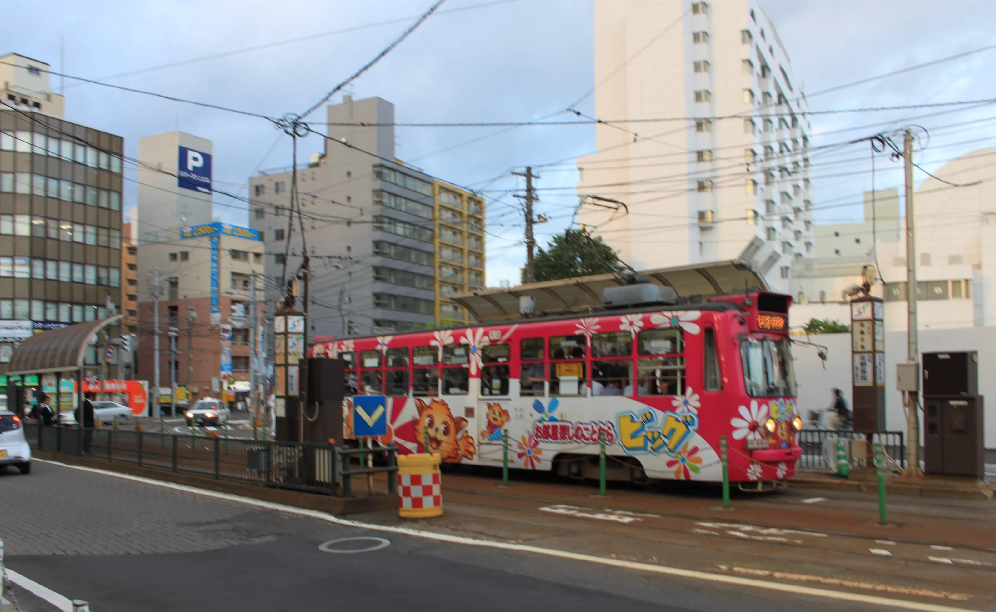 Kolorowy tramwaj jadący przez Sapporo z wieżowcami w tle