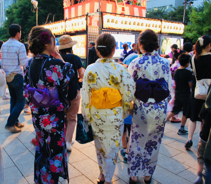 Trzy Japonki ubrane w kimono, stojące tyłem, z przychodnią w tle w Parku Odori w Sapporo