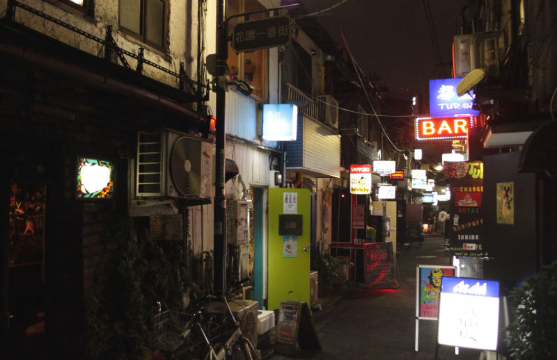 Ulica w Golden Gai nocą, z widocznymi małymi barami i kolorowymi neonami.
