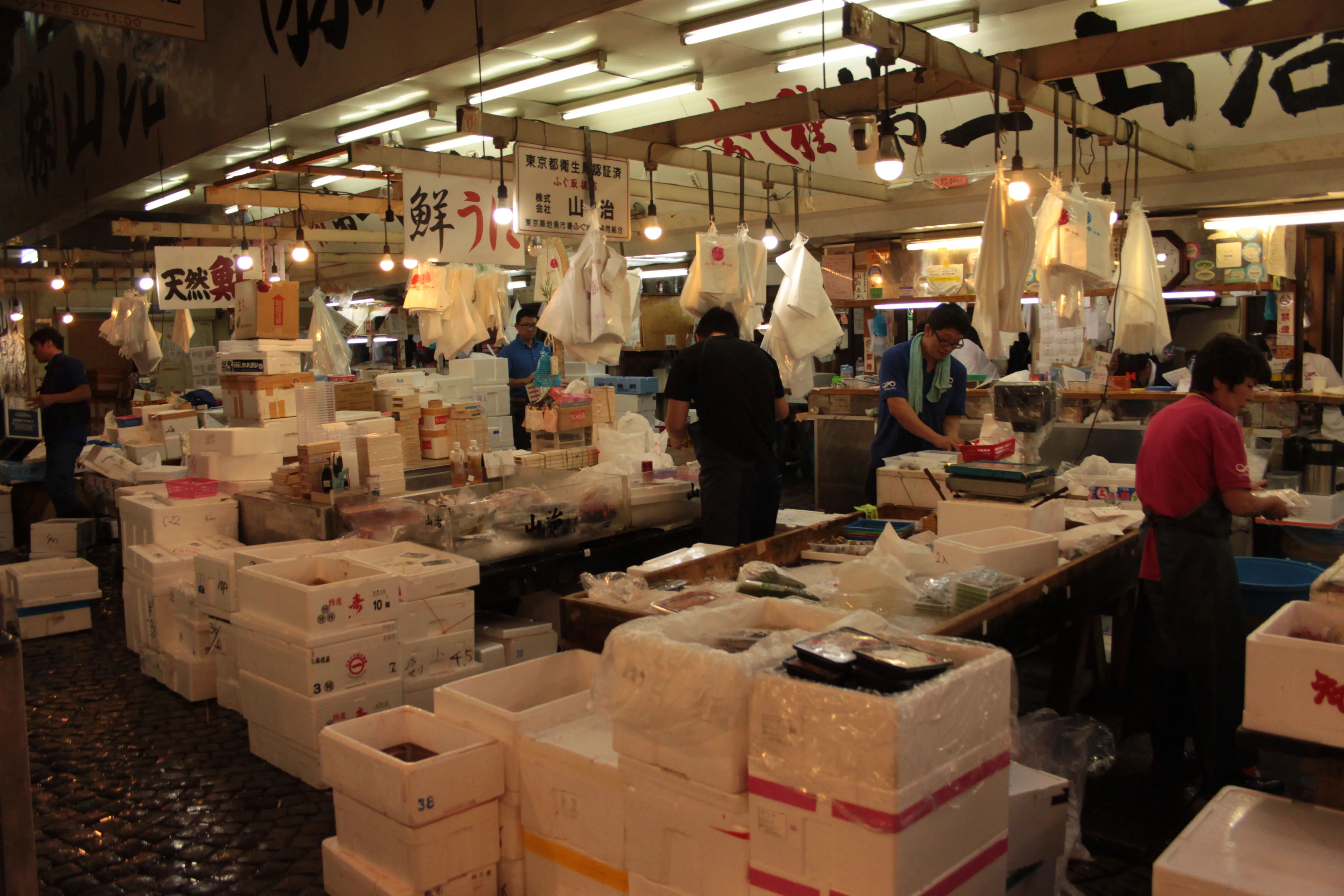 Wnętrze Tsukiji Market z widocznymi sprzedawcami i skrzyniami z owocami morza.