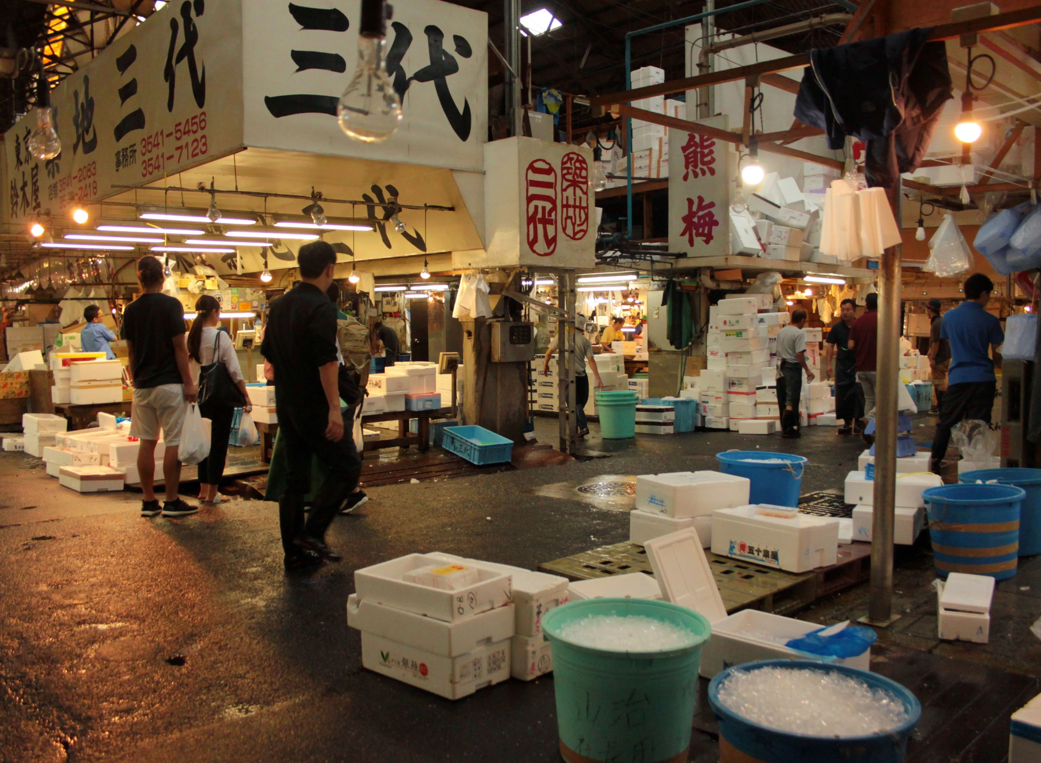 Zatłoczony rynek wewnątrz Tsukiji Market z widocznymi stoiskami pełnymi ryb i owoców morza.