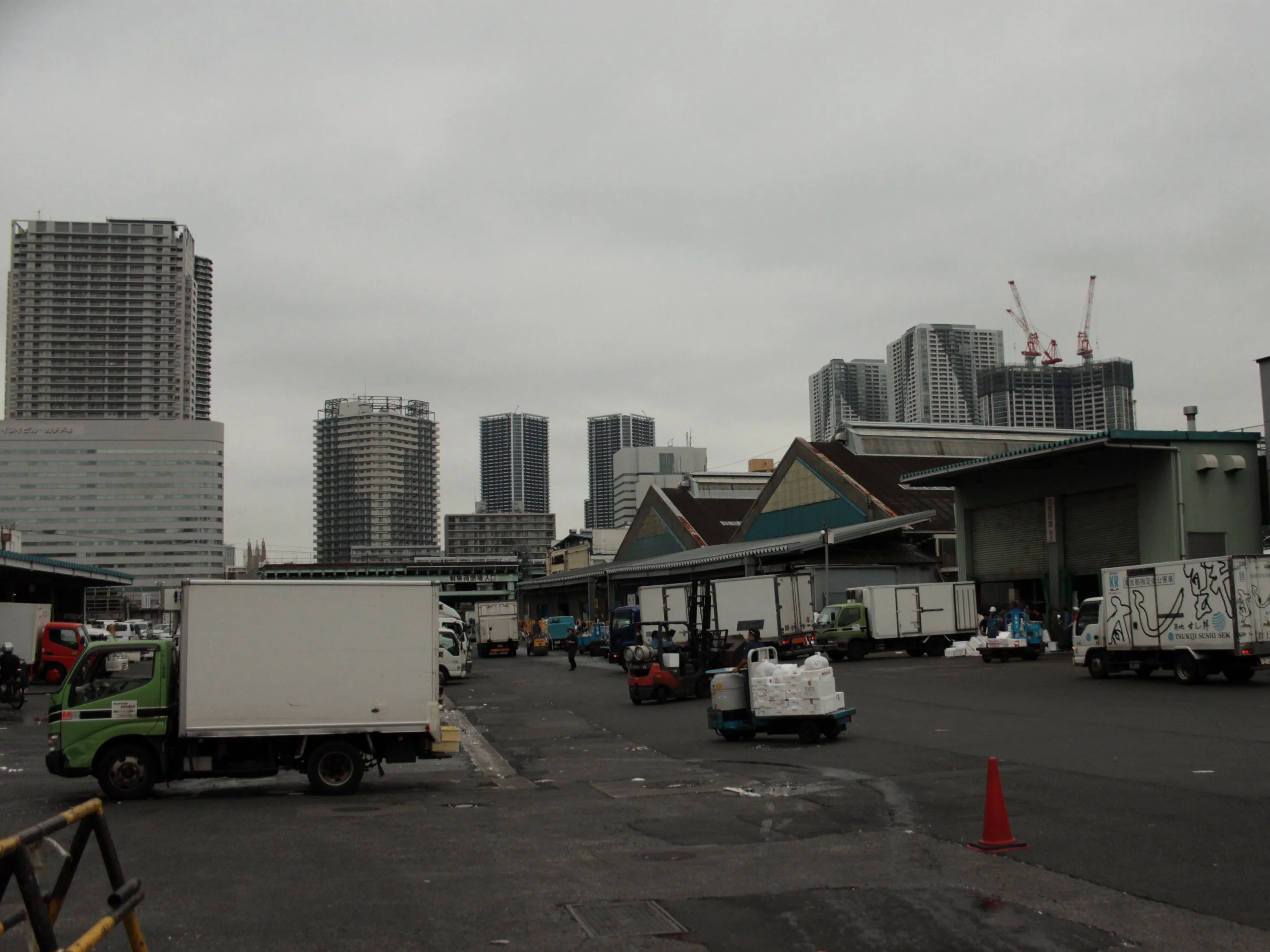 Widok na parking i magazyny przy Tsukiji Market w Tokio, z wieżowcami w tle.