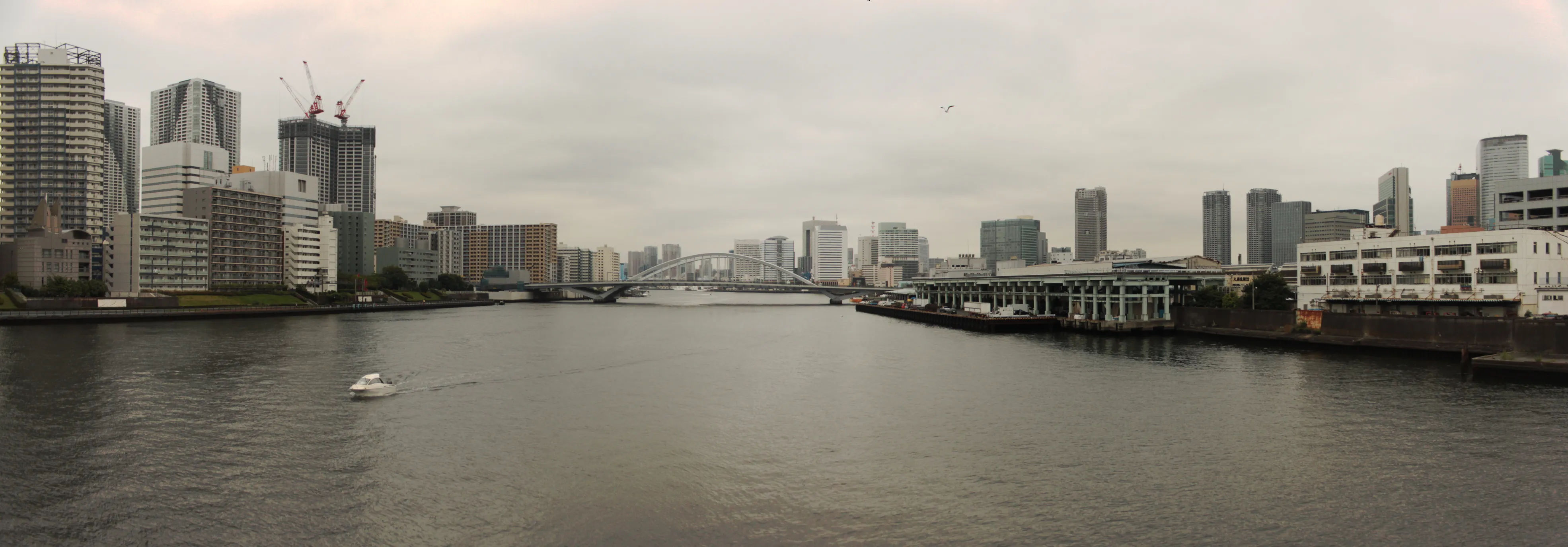 Widok na rzekę i budynki w pobliżu Tsukiji Market, przy pochmurnym niebie.