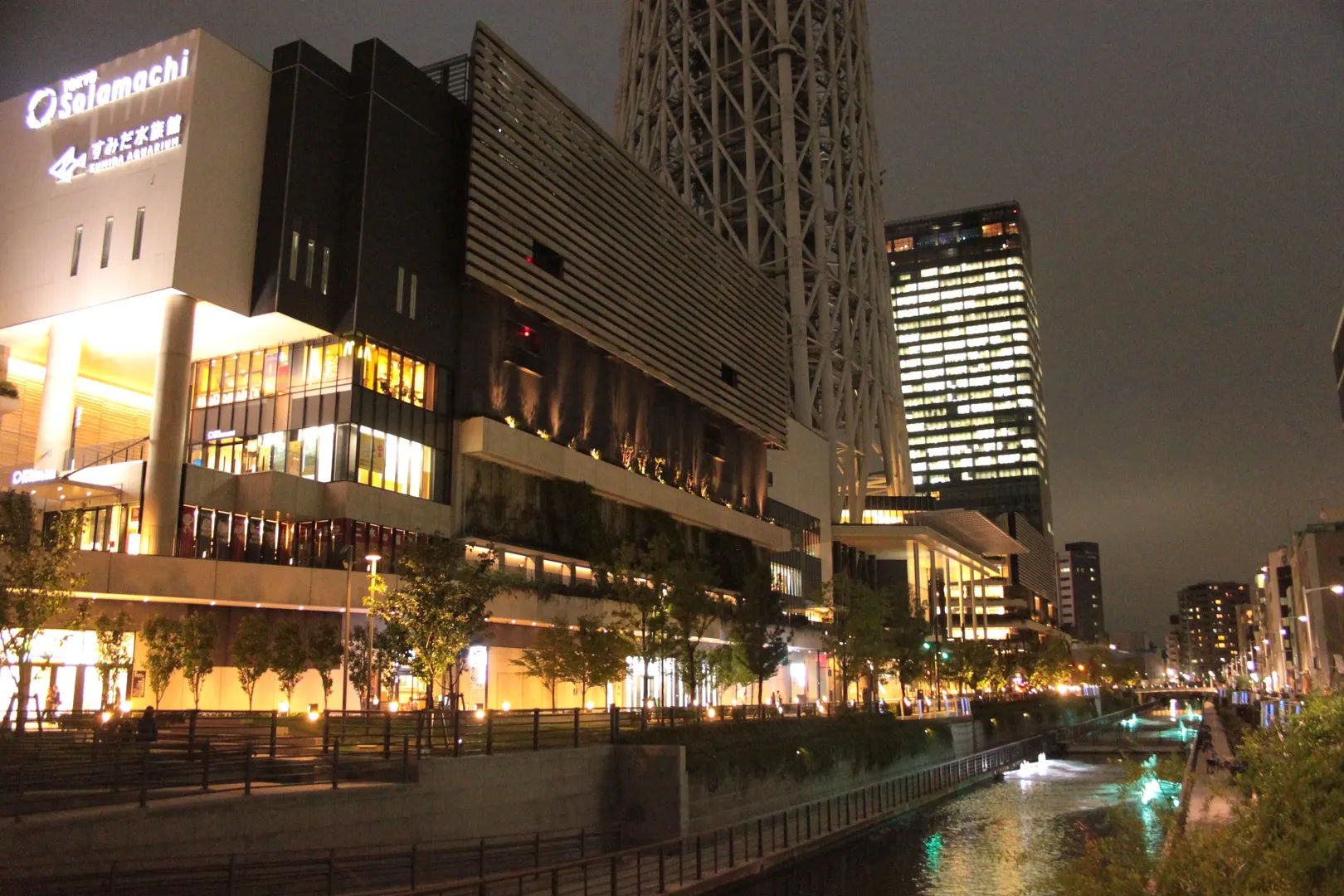 Nocny widok na kompleks Tokyo Solamachi wzdłuż kanału, z oświetlonymi budynkami.