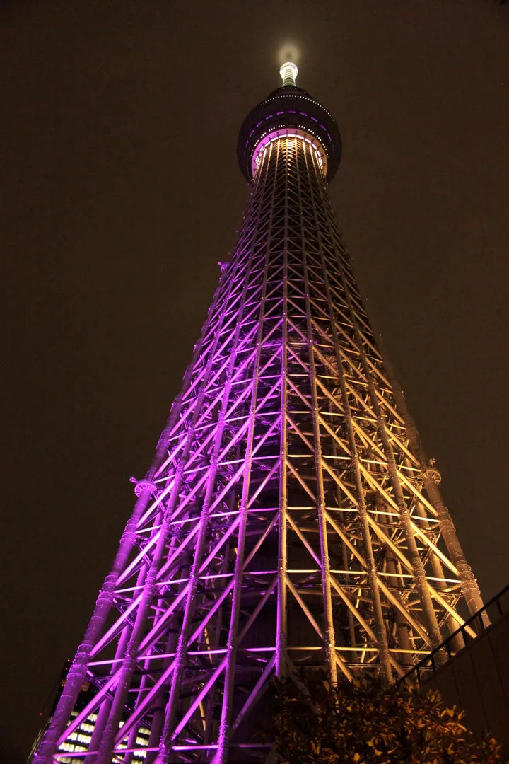 Tokyo Skytree oświetlone nocą fioletowym światłem, widok z dołu.