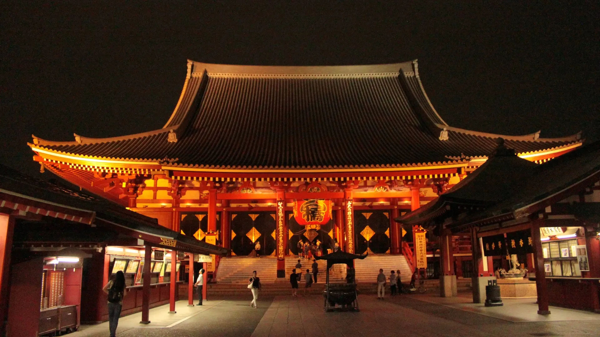 Nocny widok na główną halę świątyni Sensō-ji w Tokio, oświetloną złotymi światłami.