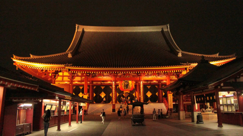 Nocny widok na główną halę świątyni Sensō-ji w Tokio, oświetloną złotymi światłami.