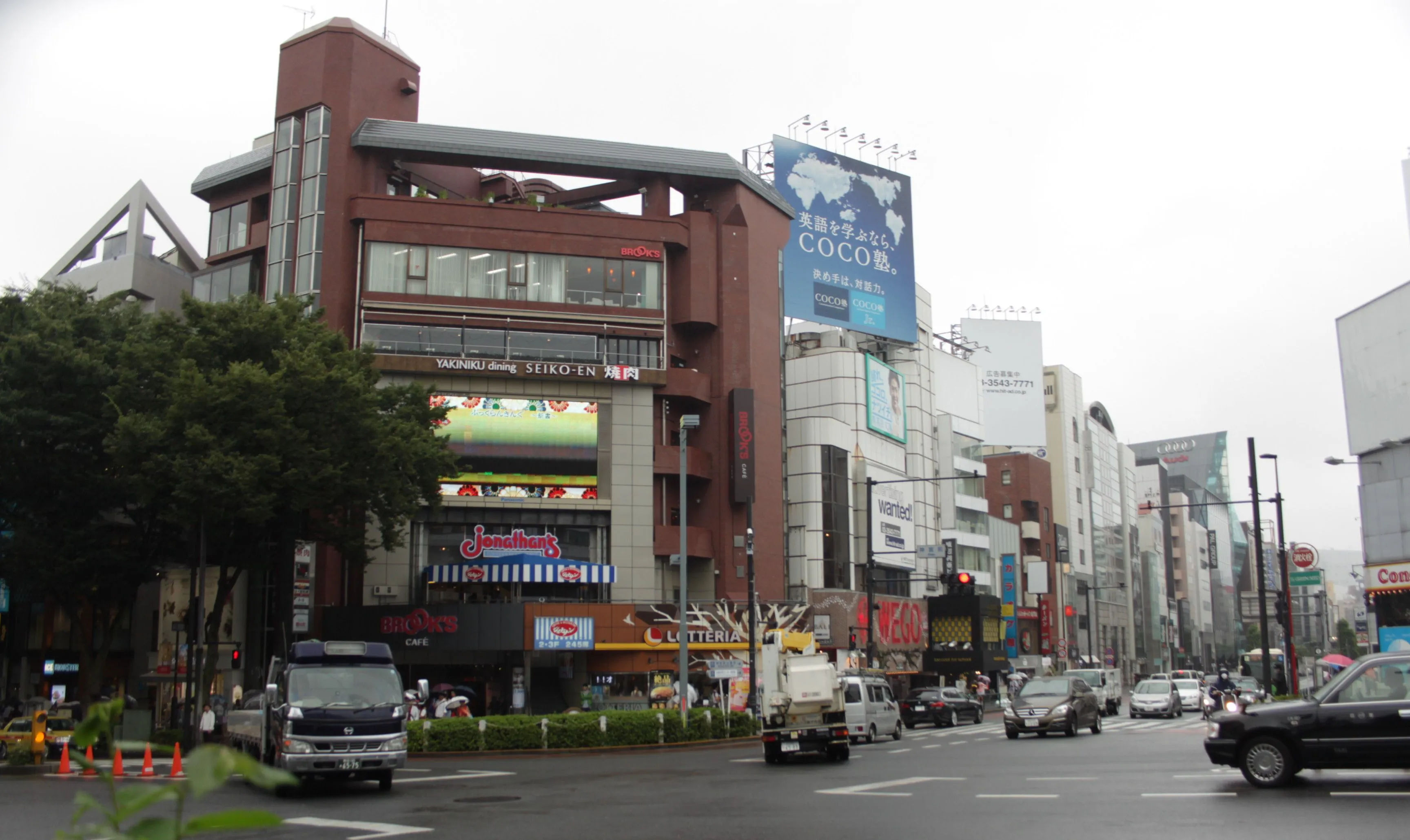 Widok na skrzyżowanie przy ulicy Omotesando w Tokio, otoczone nowoczesnymi budynkami.