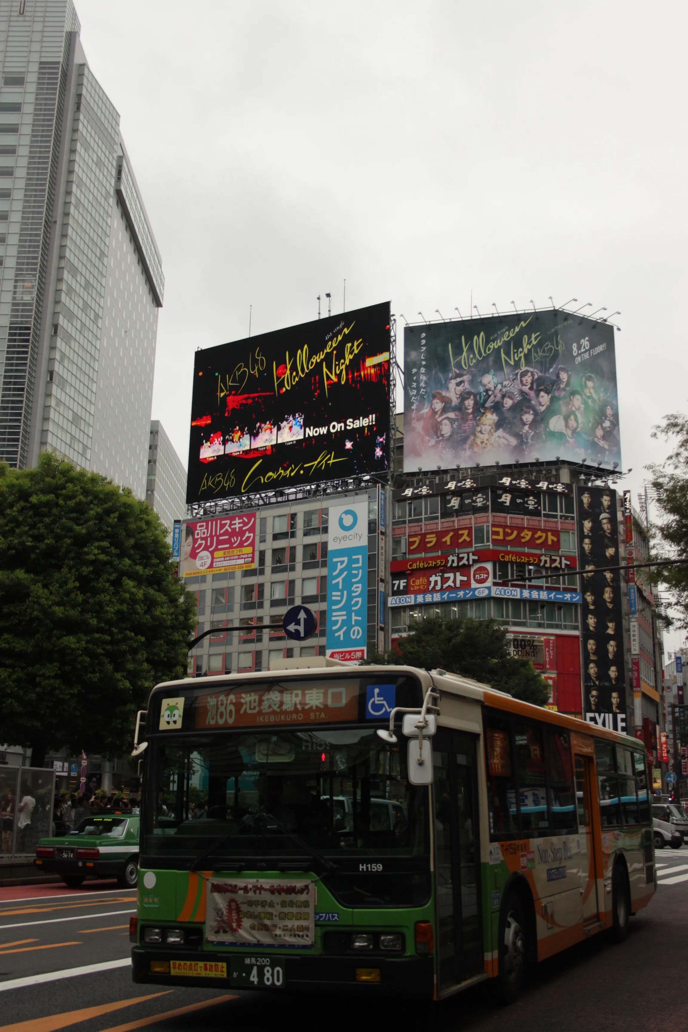 Dzień w Shibuya z widokiem na liczne reklamy i neony na budynkach przy skrzyżowaniu.