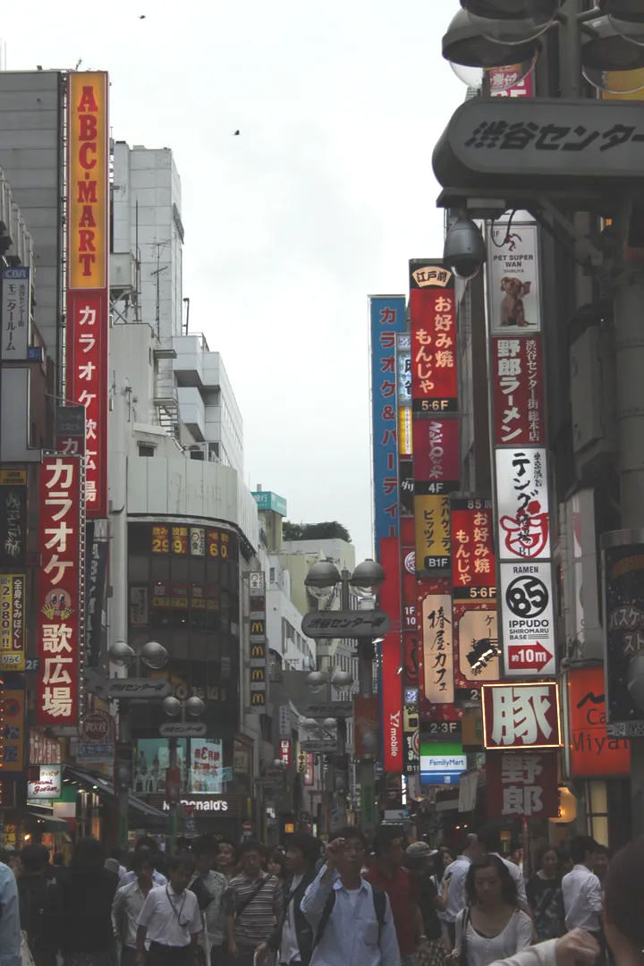 Tętniąca życiem ulica handlowa w dzielnicy Shibuya, z kolorowymi neonami i reklamami.