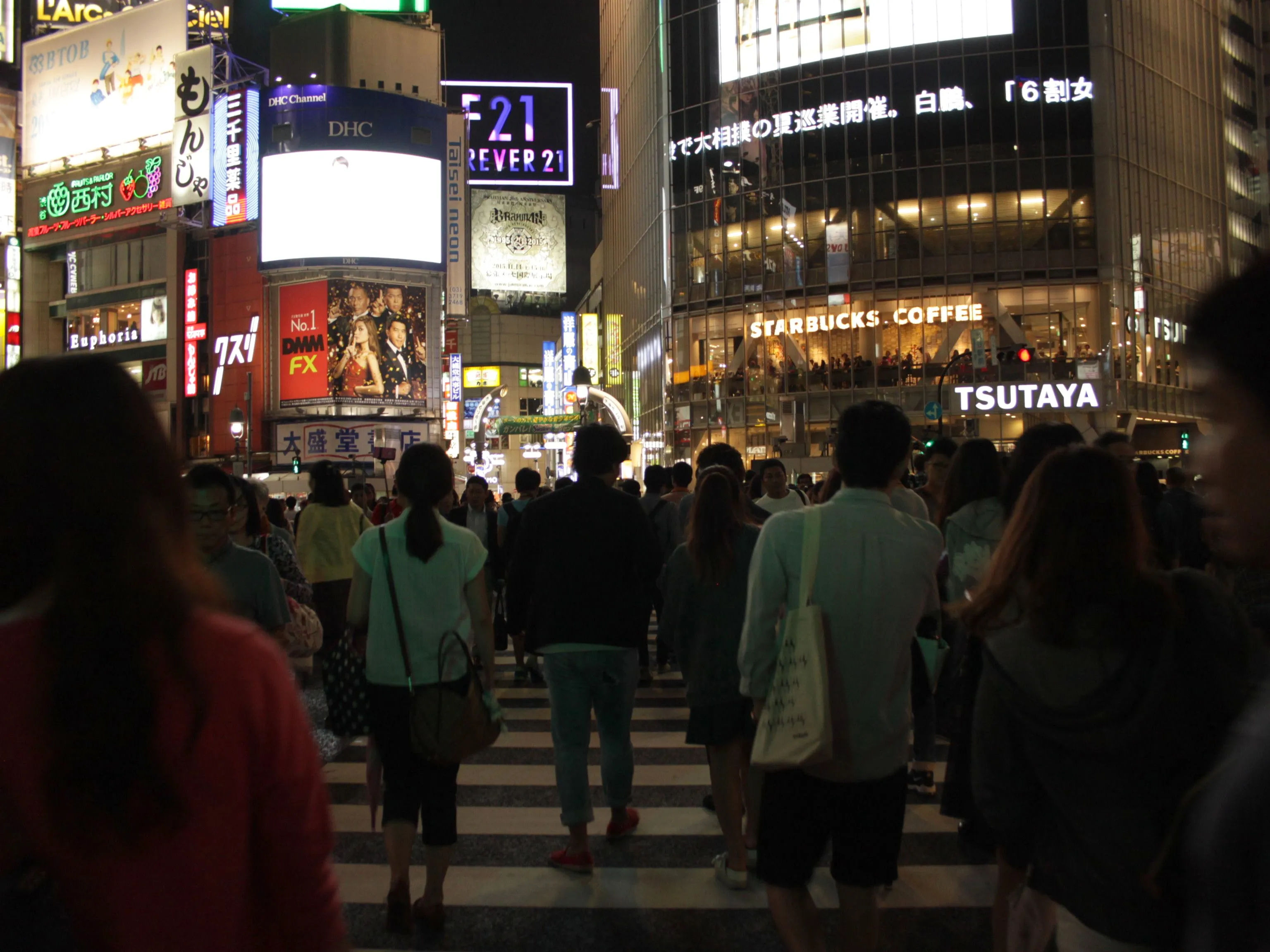 Tłum ludzi przechodzący przez skrzyżowanie Shibuya nocą, otoczony oświetlonymi budynkami.