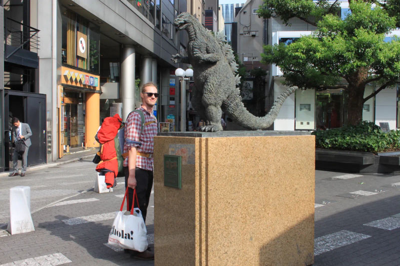 Osoba stojąca z plecakiem przy pomniku Godzilli w dzielnicy Ginza, Tokio, Japonia