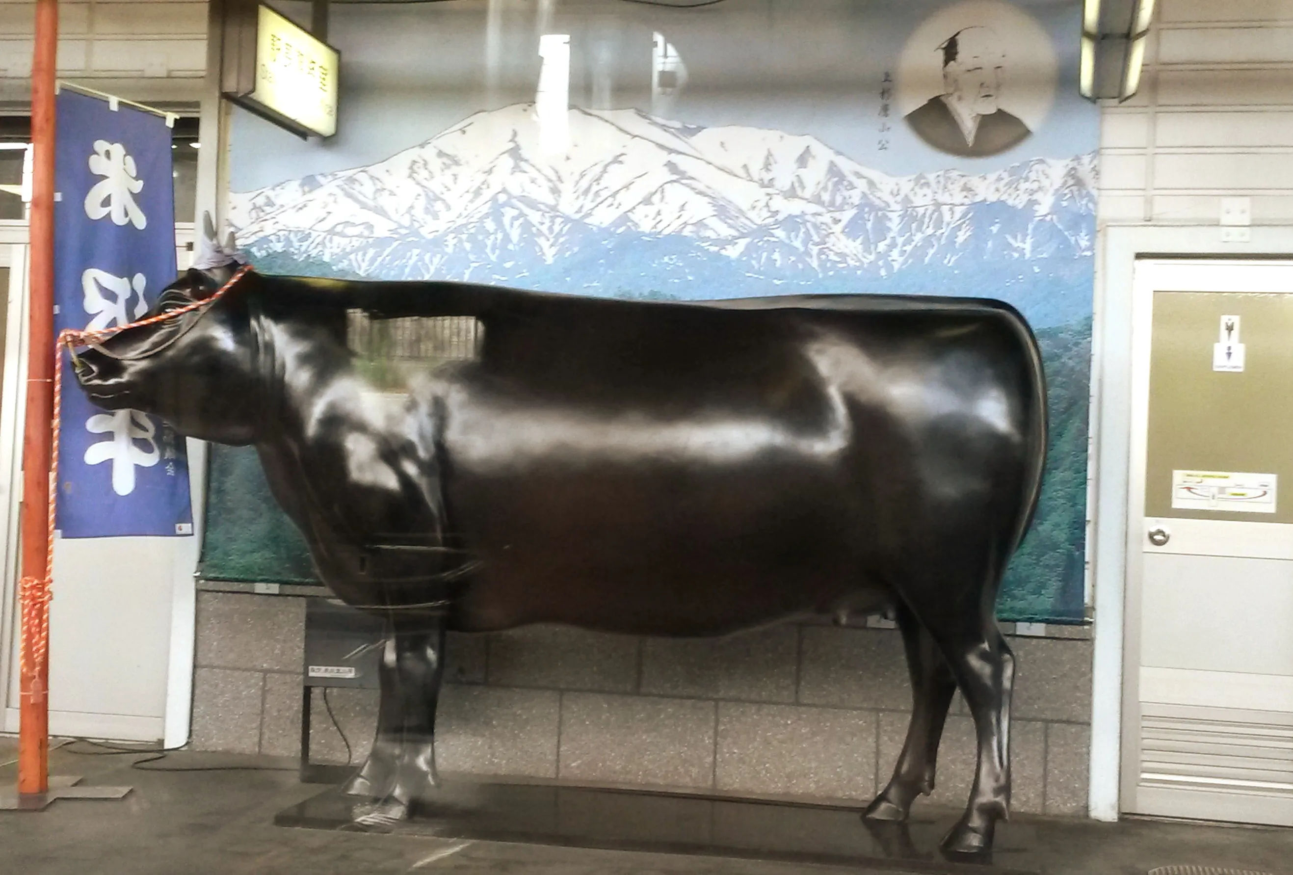 Statua czarnej krowy umieszczona na tle malowidła przedstawiającego góry w Zao Onsen, Japonia.
