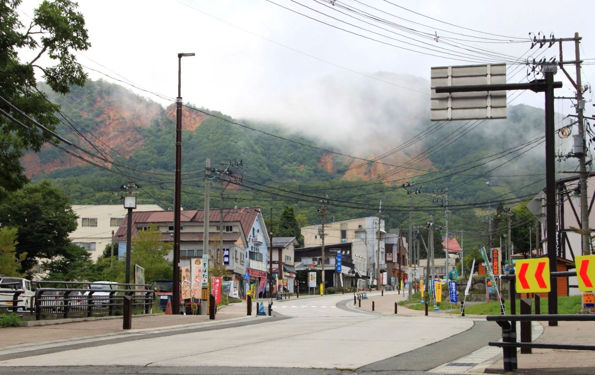 Widok na ulicę w Zao Onsen z budynkami w tle, otoczoną górami częściowo zasłoniętymi mgłą, Japonia.