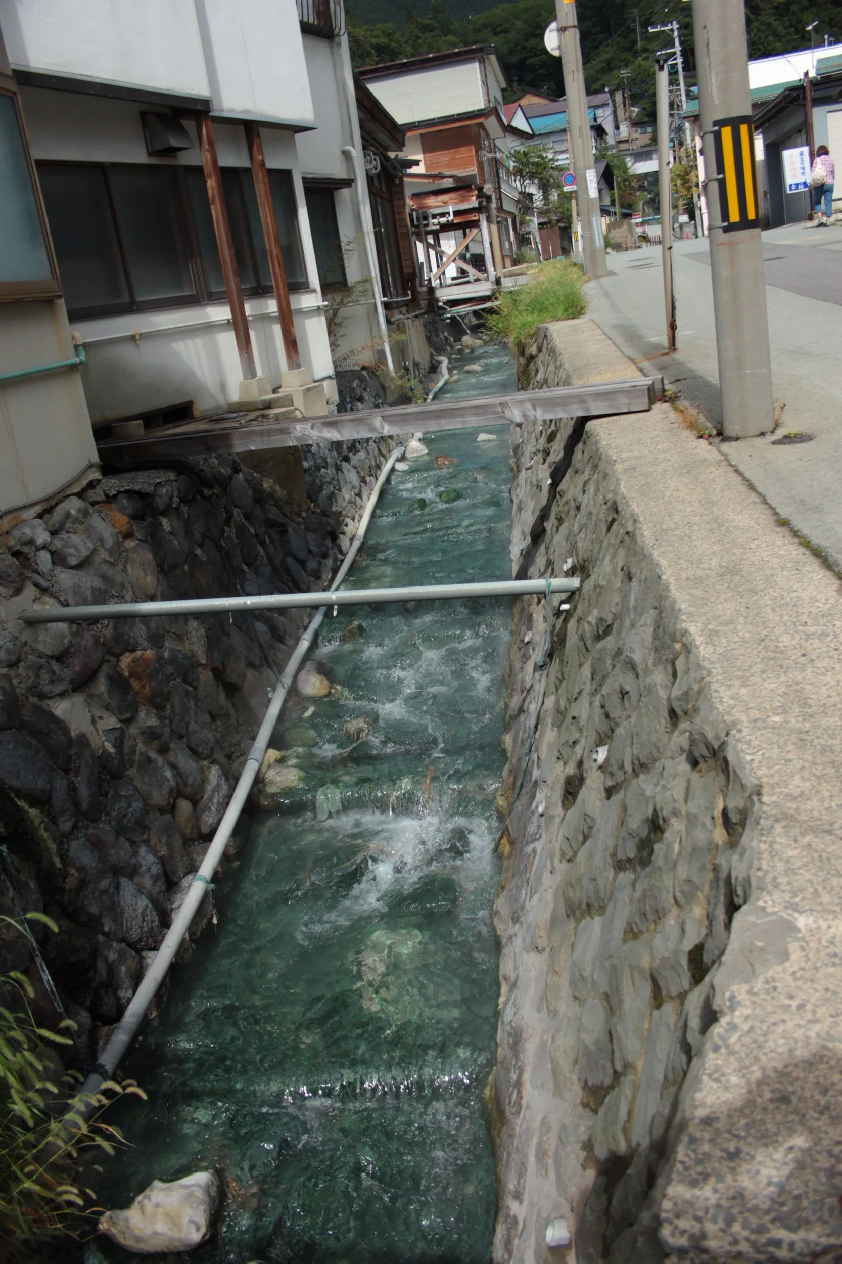 Strumień przepływający przez kamienny kanał w Zao Onsen, Japonia, otoczony tradycyjną infrastrukturą miejską.