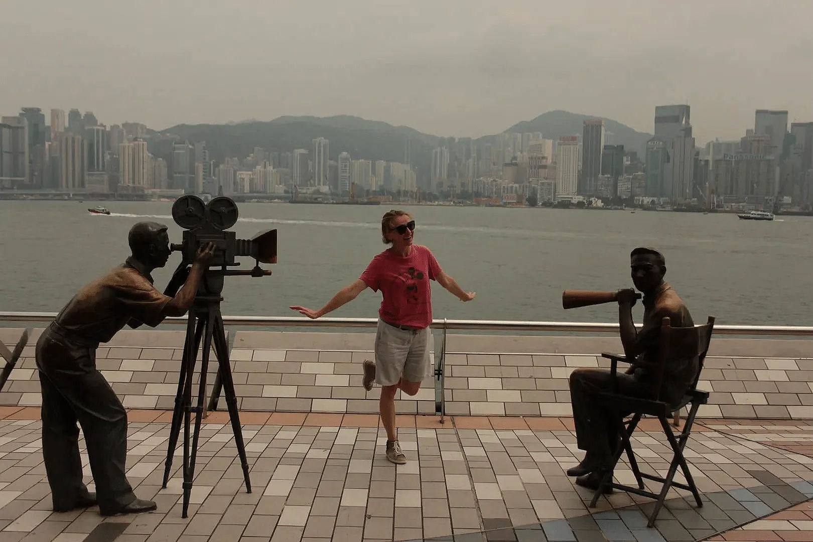 Mężczyzna pozujący przy posągach filmowców na tle zatoki w Hongkongu