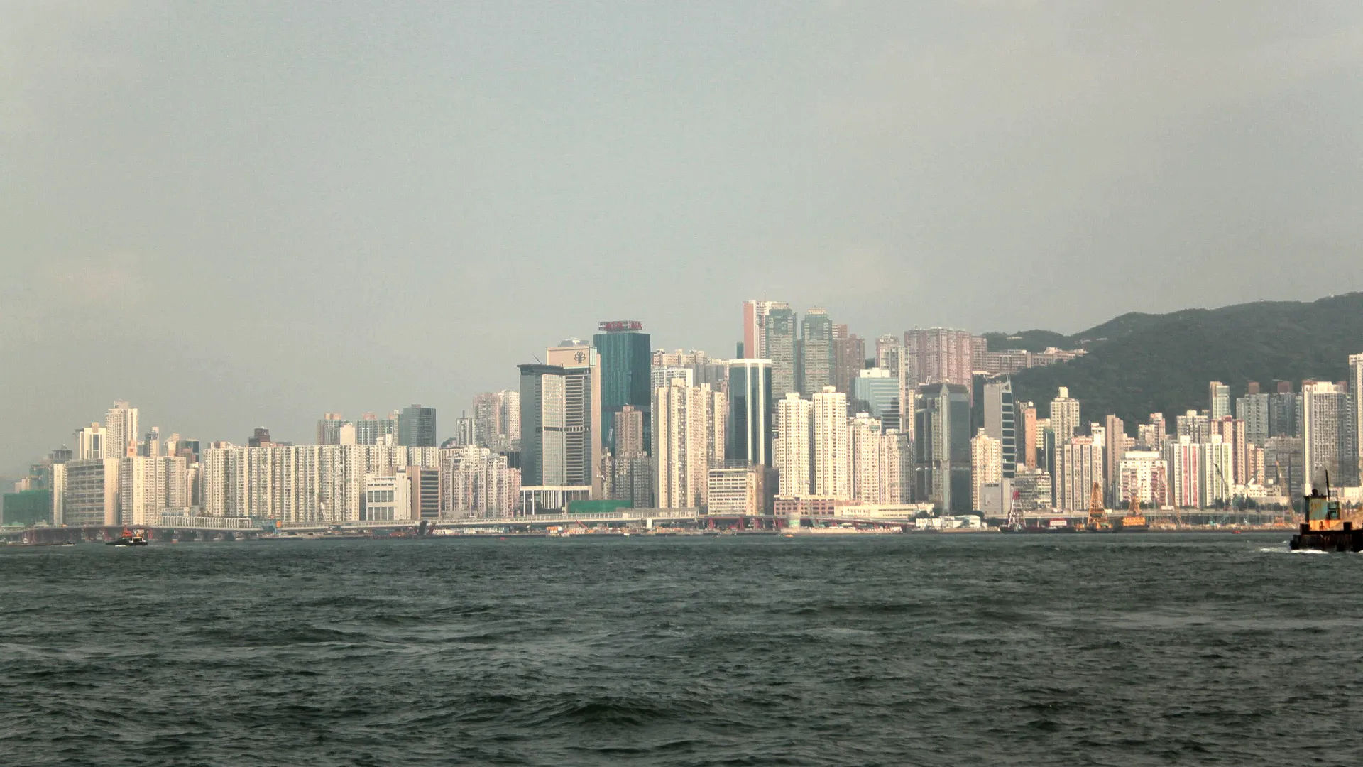 Widok na panoramę Hongkongu z wysokimi budynkami i górami w tle, morze na pierwszym planie