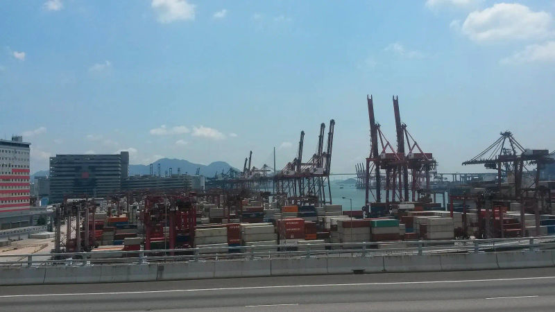 Kontenery i dźwigi portowe w porcie towarowym Hongkongu, z górskimi wyspami w tle