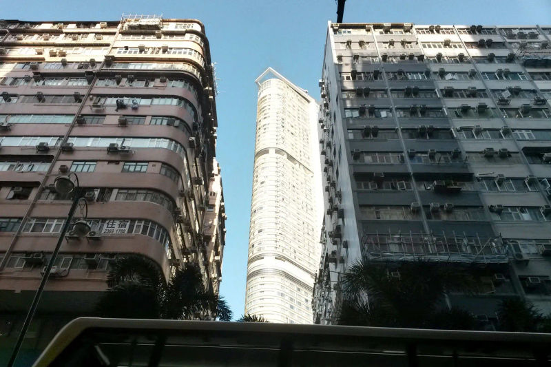 Nowoczesny wieżowiec między dwoma starszymi budynkami mieszkalnymi w dzielnicy Kowloon, Hongkong