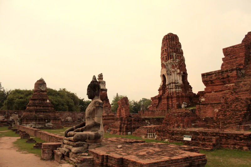 Wat Mahathat w Ayutthayi – posąg Buddy na tle ceglanej prang w historycznym parku Tajlandii
