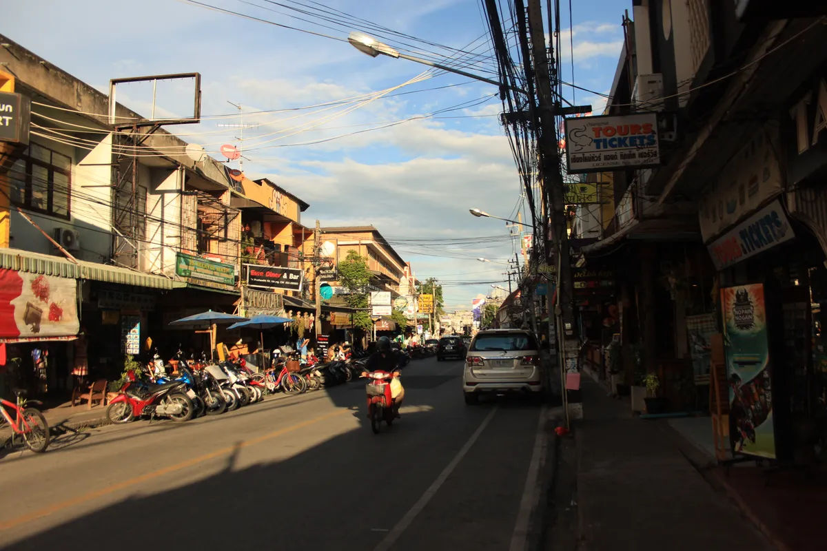 Tradycyjna ulica z wąską drogą w Chiang Mai, pełna tuk-tuków i lokalnych sklepów.