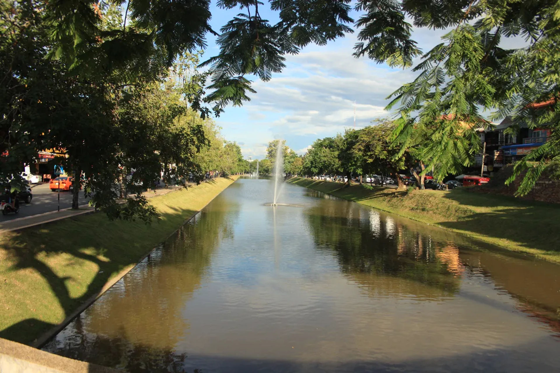 Kanał z wodą i fontanna w Chiang Mai, z zielonymi drzewami wokół.