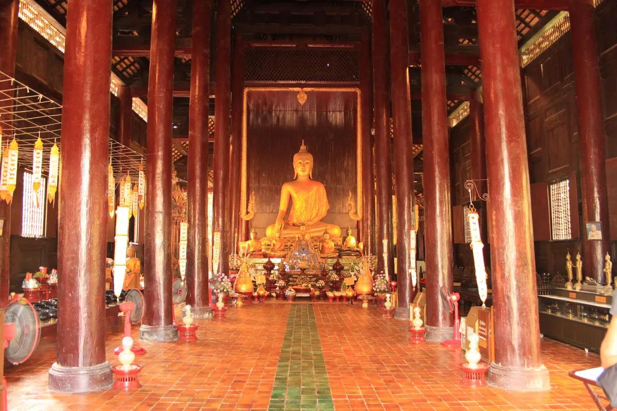 Wnętrze świątyni Wat Phan Tao w Chiang Mai z widokiem na złoty posąg Buddy.
