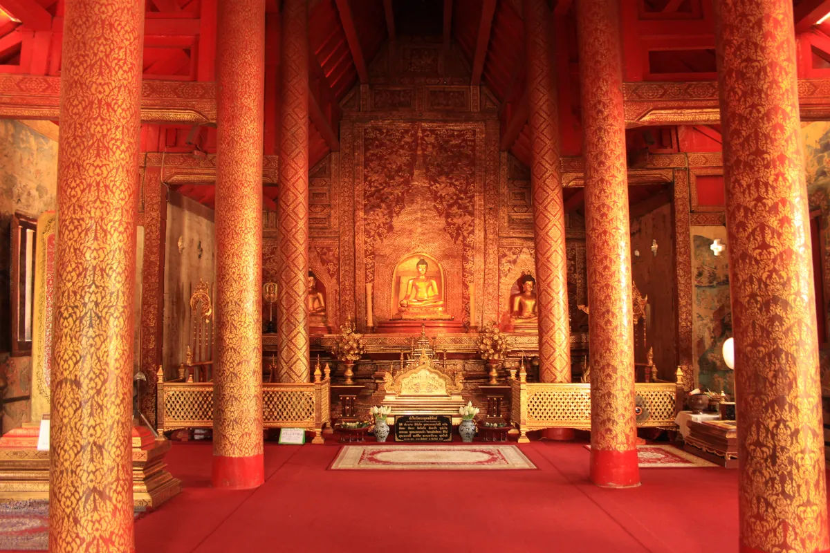 Wnętrze świątyni Wat Phra Singh, z centralnym posągiem Buddy otoczonym zdobionymi kolumnami.