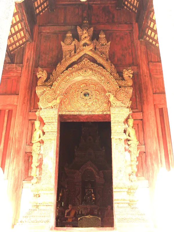 Złocone wejście do świątyni Wat Phra Singh w Chiang Mai, ozdobione bogatymi detalami rzeźbiarskimi.