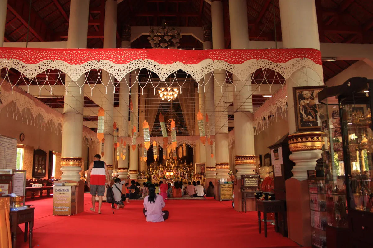 Wnętrze świątyni Wat Phra Singh w Chiang Mai, Tajlandia, z widokiem na złoty posąg Buddy otoczony zdobionymi kolumnami.