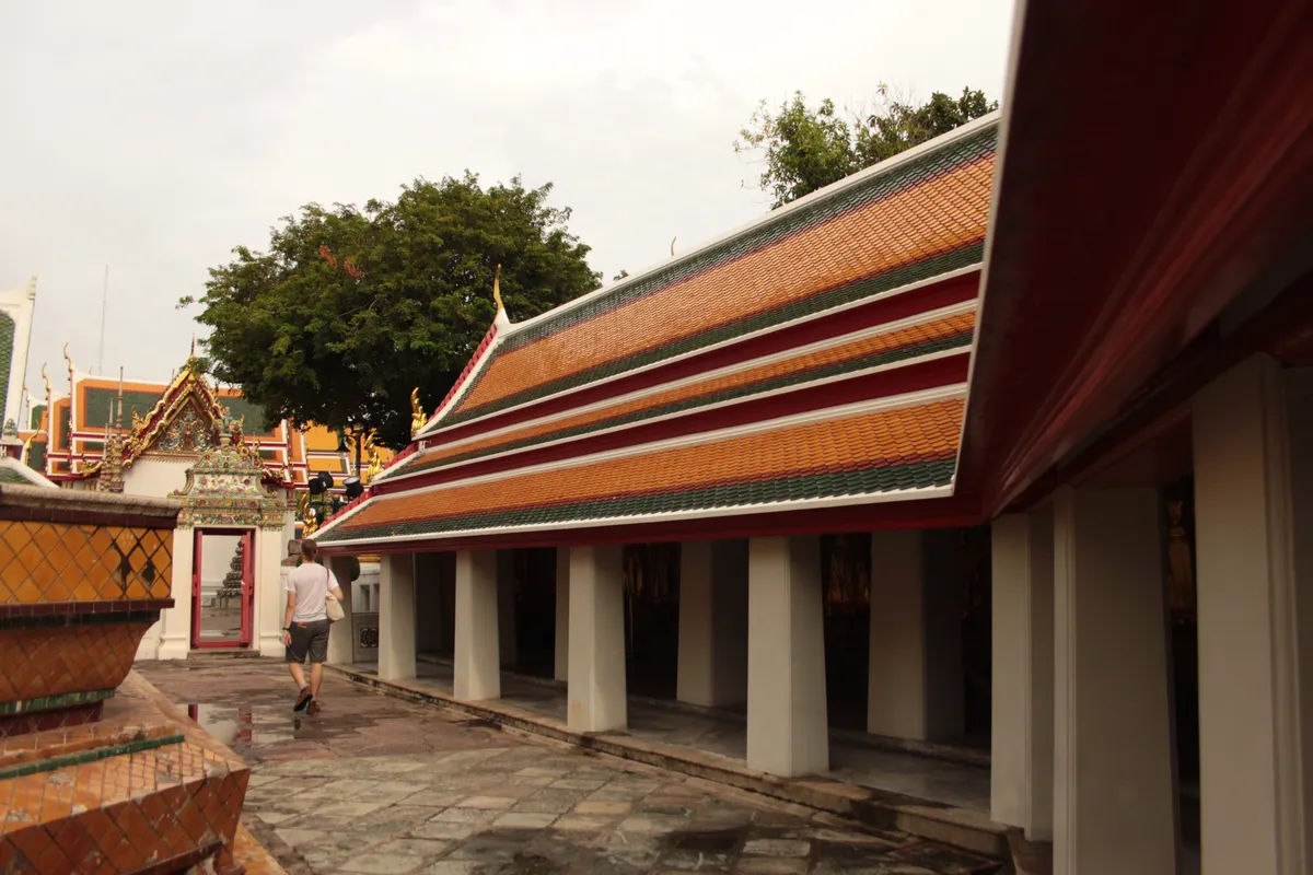 Szczegóły dekoracji w Wat Pho, z kamiennymi postaciami w tle.
