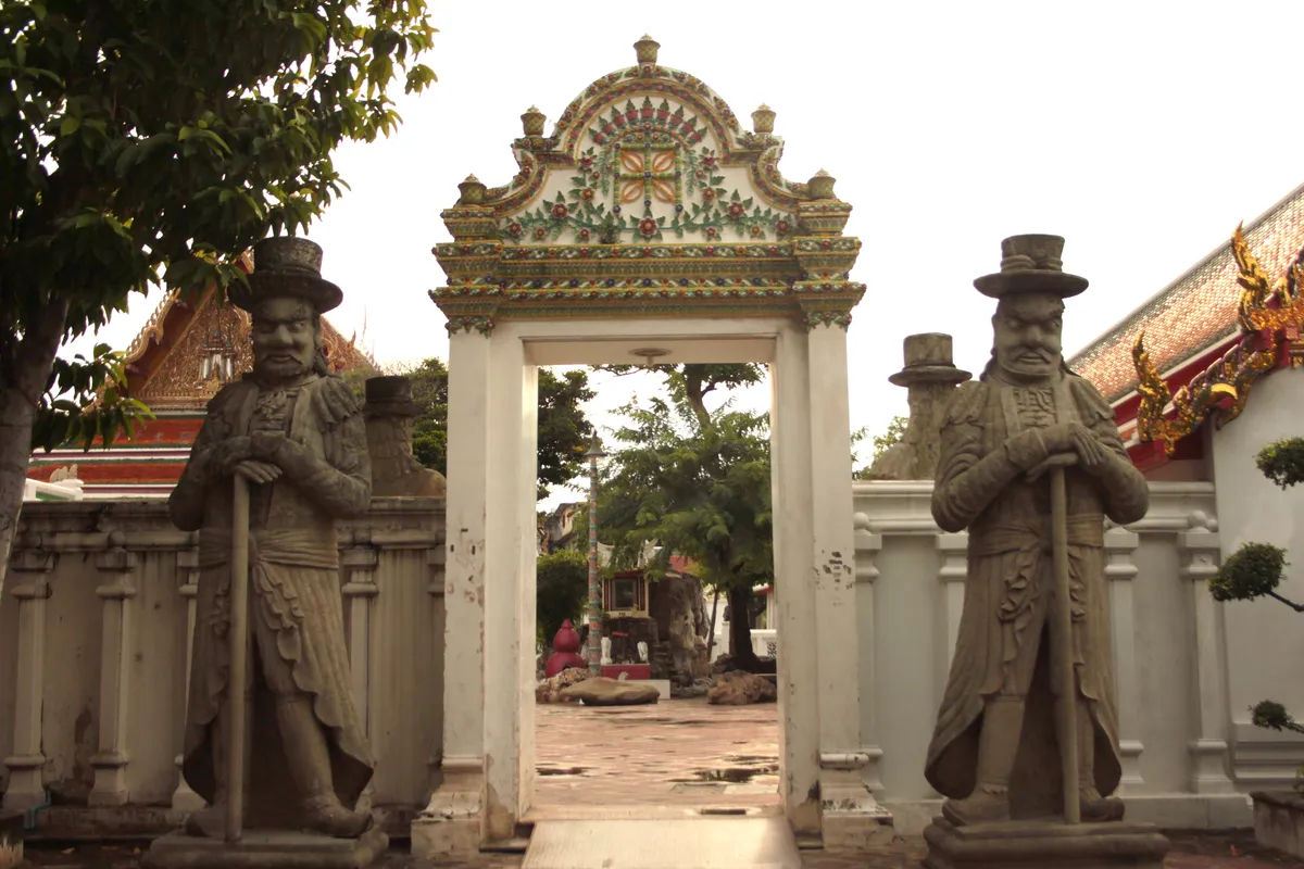 Posągi strażników przy wejściu do Wat Pho w Bangkoku, z tajską architekturą w tle.