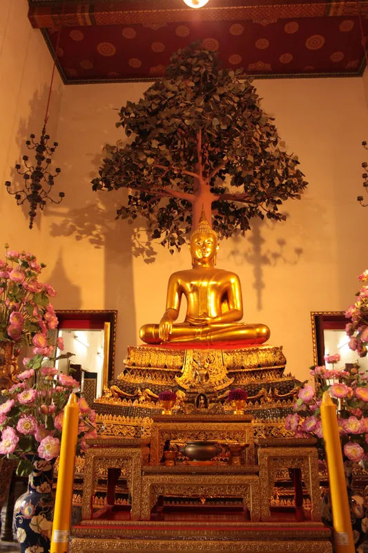Złoty posąg Buddy w Wat Pho w Bangkoku, ozdobiony wokół kwiatami i dekoracjami.