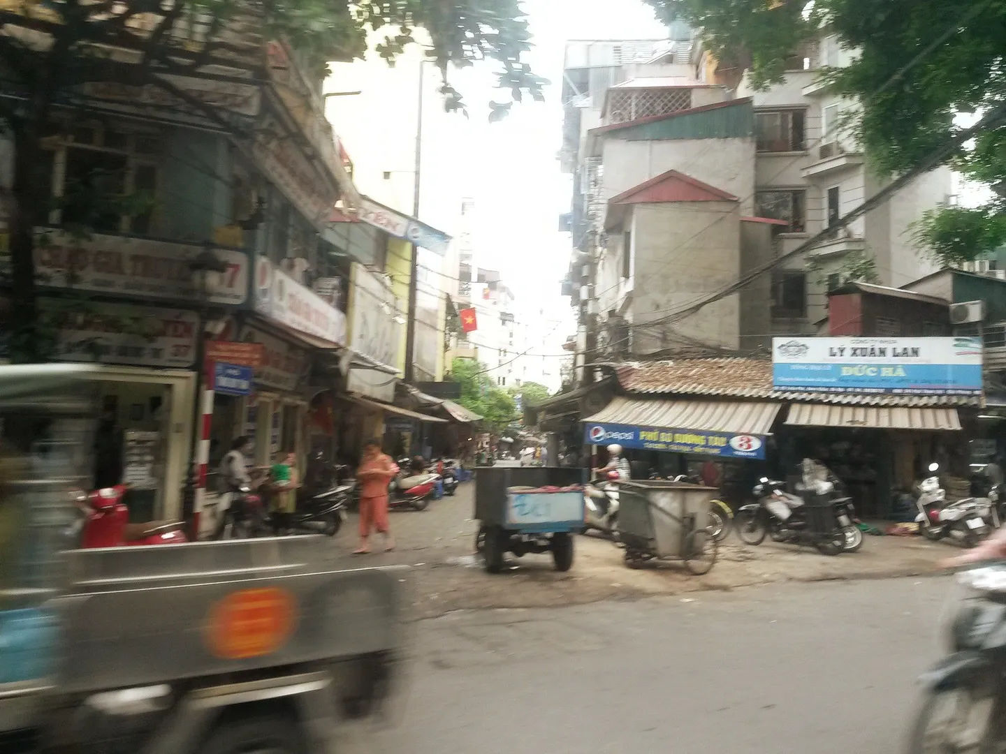 Ulica w Starej Dzielnicy Hanoi z motocyklistami i lokalnymi sklepami po bokach