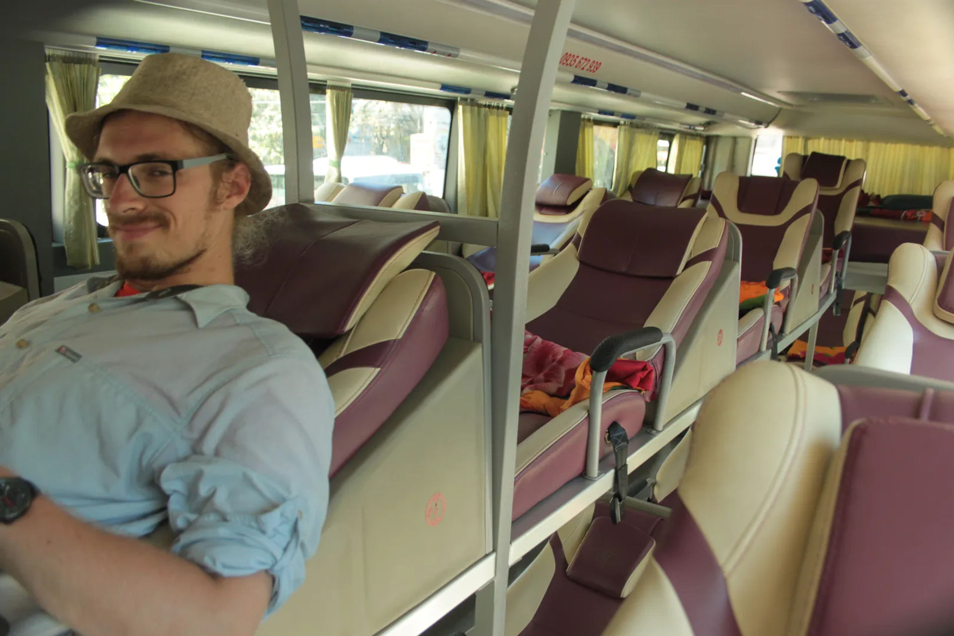 Podróżnik w okularach i kapeluszu relaksujący się w komfortowym, rozkładanym siedzeniu autobusu sypialnego w Wietnamie.