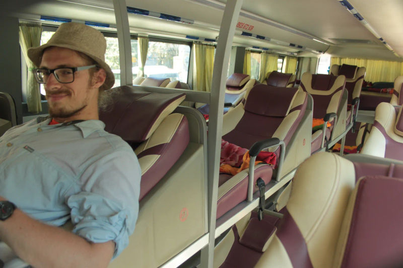 Podróżnik w okularach i kapeluszu relaksujący się w komfortowym, rozkładanym siedzeniu autobusu sypialnego w Wietnamie.