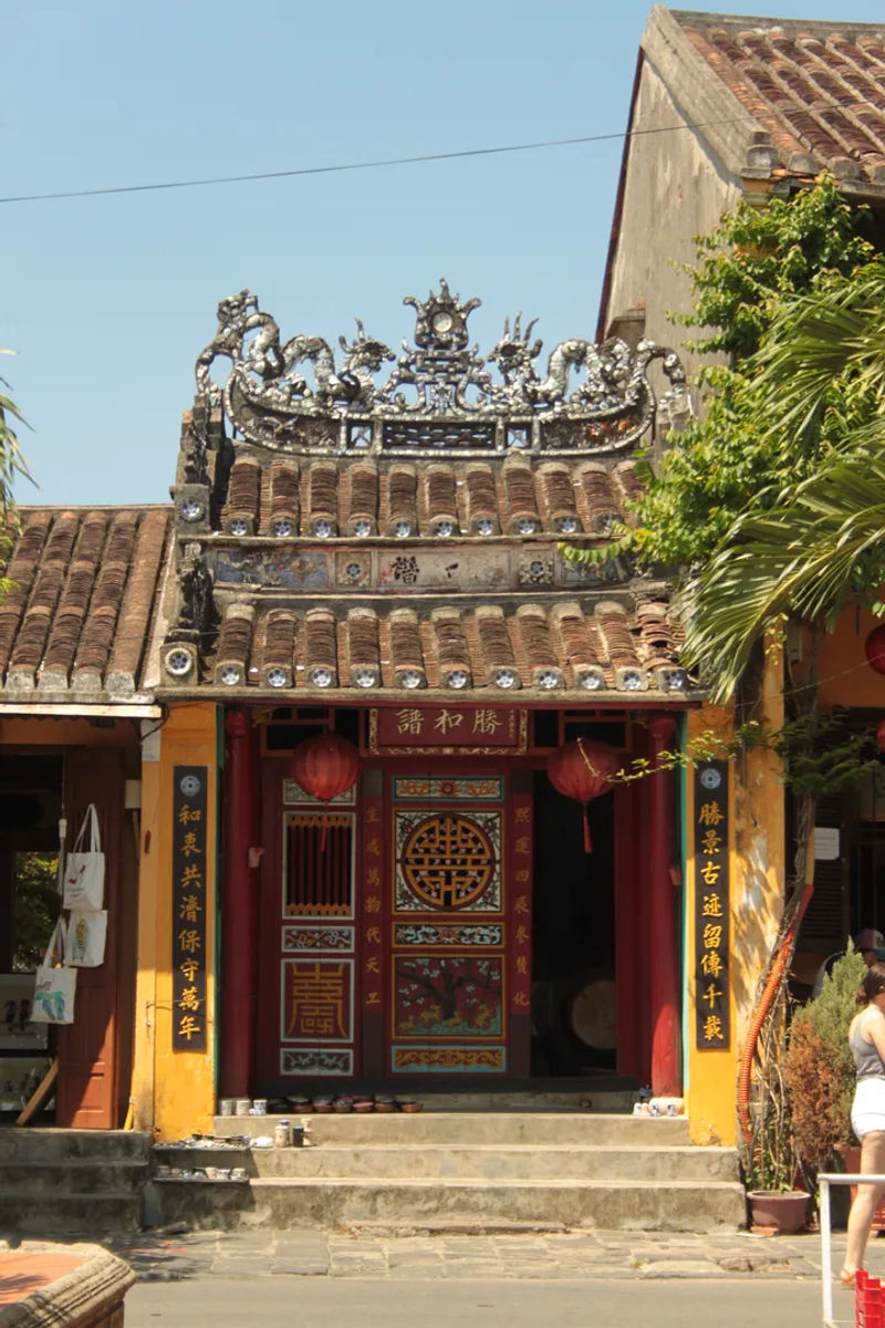 Zabytkowy budynek świątynny z ozdobnym dachem i czerwonymi lampionami na tle bujnej roślinności, Hoi An, Wietnam.