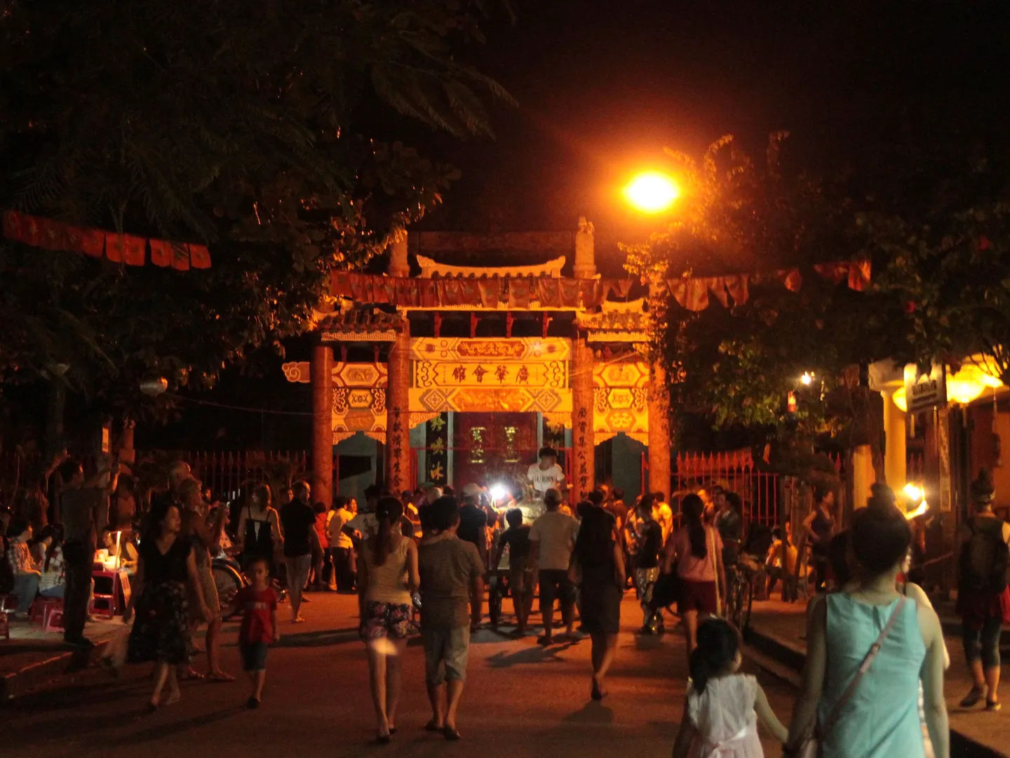 Tłum ludzi przed ozdobną, oświetloną bramą podczas nocnych obchodów, Hoi An, Wietnam.